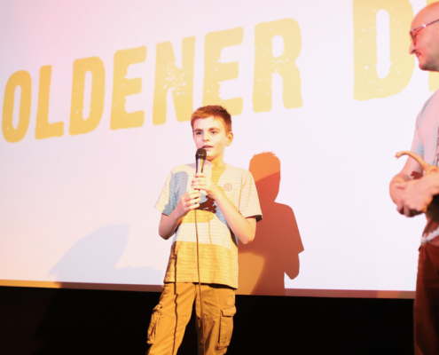 Ein Junge steht mit einem Mikrofon vor einer großen Kinoleinwand