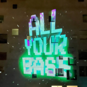 Projektion des Schriftzugs ALL YOUR BASE auf einer urbanen Hauswand.